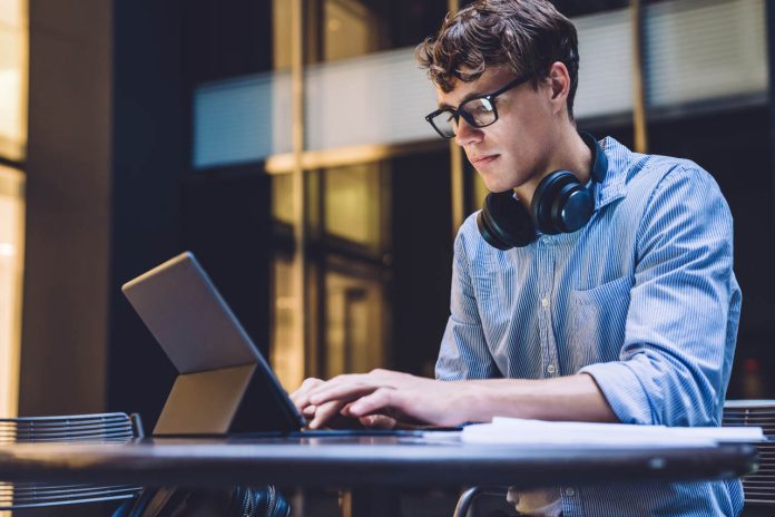 Young,Handsome,Concentrated,Man,In,Glasses,With,Headphones,Browsing,Ultrabook